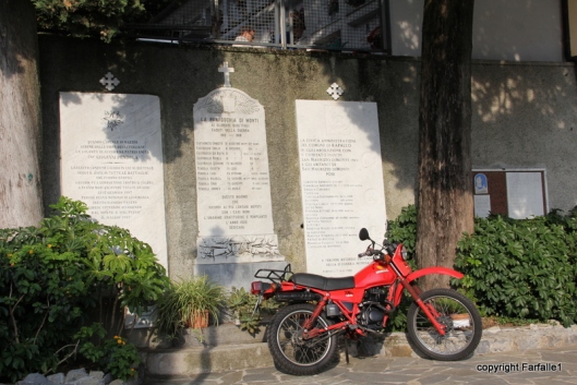 Red motorcycle in front of tablets commemorating war dead.